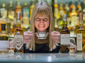 Julie Trevisan Hunter holding a whisky quaich with bottles of whisky on the table