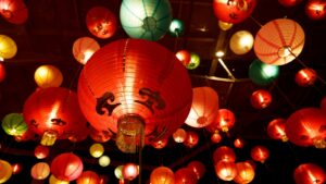 Image of red, orange, yellow and green Chinese lanterns hanging amongst a dark background.