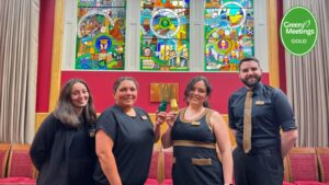 Group of four people raising a toast to an award standing in front of a stained glass window.
