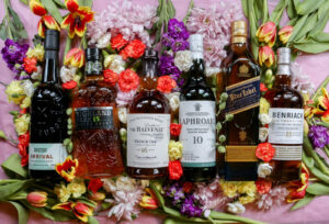 Women in Whisky themed whiskies of the month, 6 bottles of whisky with pink background with colourful flowers.