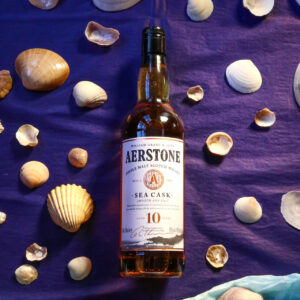 Bottle of Aerstone Sea Cask pictured on a two tone background of light and dark blue, surrounded by sea shells.