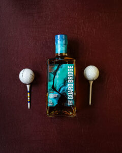 A bottle of The Guard Bridge. Pictured on a maroon leather background with gold balls and tees.