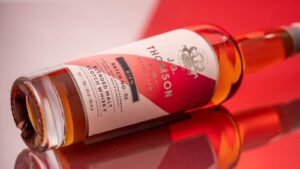 A bottle of JG Thompson Rich Blended whisky pictured on a white and red background.