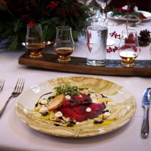 A dish of cured trout pictured with a whisky flight in a festive scene.