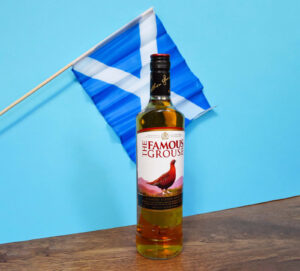 Bottle of The Famous Grouse and a Scottish flag against a blue background.