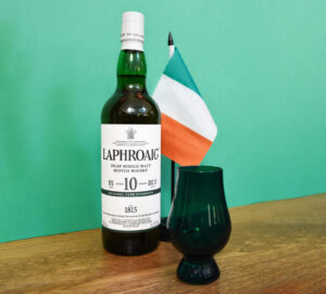 Bottle of Laphroaig 10 Scotch Whisky with an Irish flag and green Glencairn glass against a green background.