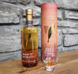 Bottle of Man O'Words Scotch Whisky, bottle case and a dram against a stone backdrop.