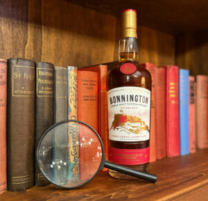 Bottle of Bonnington Scotch whisky next to a magnifying glass on a book shelf.