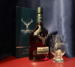 Bottle of Dalmore whisky with a Glencairn glass against a navy curtain.