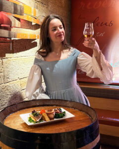Cast member holding a dram of whisky next to a plate of food.
