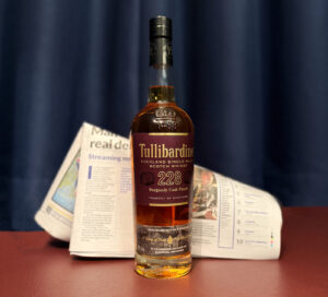 Bottle of Tullibardine and newspaper against a navy curtain