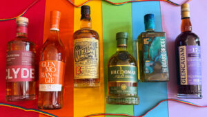 Six bottles of Scotch whisky against a rainbow background with rainbow laces.