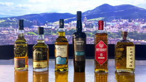 Six bottes of Scotch Whisky against a backdrop showing a landscape of Edinburgh and Arthur's Seat.