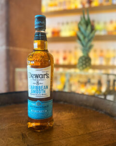 Bottle of Dewar's Caribbean Smooth on a barrel accompanied with a pineapple with bar in the background.