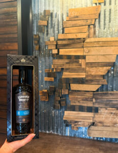 Bottle of Edinburgh Whisky Islay against a wooden map of Scotland.