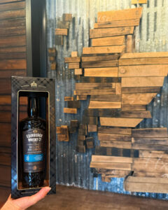 Bottle of Edinburgh Whisky Islay against a wooden map of Scotland.