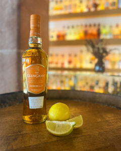 Bottle of Glen Grant Arboralis on a barrel accompanied with lemon wedges with bar in the background.