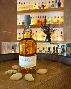 Bottle of Glenkinchie 12 on a barrel surrounded by biscuits with bar in the background.