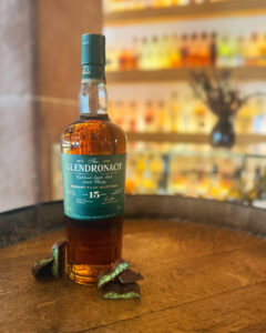 Bottle of Glendronach on a barrel accompanied with chocolate with bar in the background.