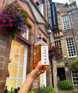 Bottle of Raasay whisky outside The Scotch Whisky Experience with flower baskets in the background.