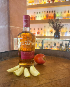 Bottle of Tomatin on a barrel surrounded by apple slices with bar in the background.