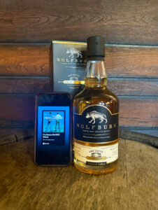 Bottle of Wolfburn whisky on a barrel with a iPhone playing The Proclaimers.