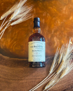 Bottle of Balvenie Scotch Whisky on an Amber coloured table with barley.