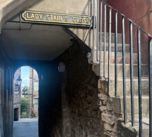 Image of Ladies Stair Close in Edinburgh showing steps on the righthand side and a dark close on the left side. At the end of the close is The Writer's Museum