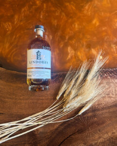 Bottle of Lindores Scotch Whisky on an Amber coloured table with barley.
