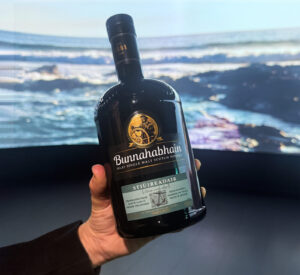 Bottle of Bunnahabhain Stiuireadair Scotch whisky against a projectin of crashing waves.