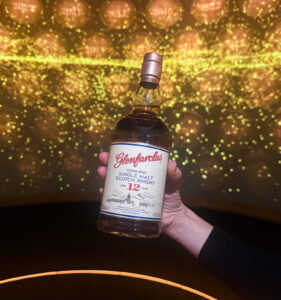 Bottle of Glenfarclas 12 Scotch Whisky held up against a projection of yellow and gold lights.