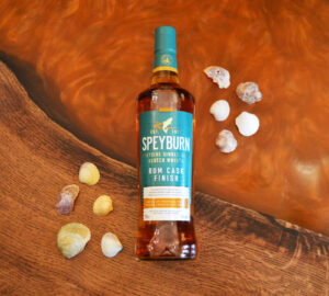 Bottle of Speyburn Rum Cask Scotch whisky on an amber table with sea shells surrounding the bottle.