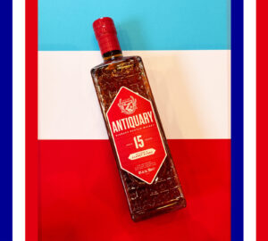Bottle of Antiquary 15 Scotch whisk yon top of a white, blue and red striped background with a border of French flags.