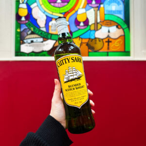 Bottle of Cutty Sark Scotch whisky held up against a red wall and stain glass window.