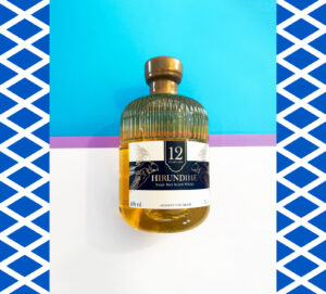 Bottle of Hirundine 12 Scotch whisky on top of a blue, white and purple background with a border of Scottish flags.