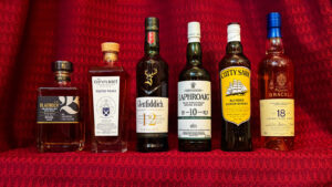 Six bottles of Scotch whisky in front of a red curtain backdrop.