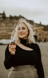 Headshot of female holding a glass of whisky in front of Edinburgh Castle.