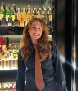 Headshot of female staff member smiling in front of a whisky collection.