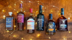 Six bottles of Scotch whisky are placed on amber table with fairy lights.