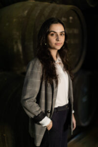 Head shot of a female SWE alumni smiling to the camera in front of a black backdrop. She is wearing a grey pin stripe suit jacket and white shirt.