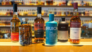 Six bottle of Scotch whisky are placed in front of a lit up whisky bar.