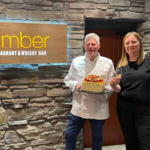 Amber Restaurant Executive Chef and Head of Events holding a cake next to Amber sign
