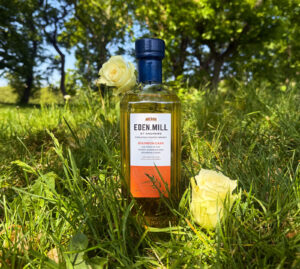 Bottle of Eden Mill Bourbon Cask sitting in the grass with two white roses. There is a park and trees in the background.