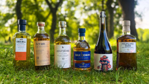 Bottle of six Scotch whiskies placed on greass with trees in the background.