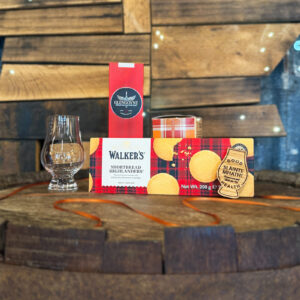 Image of corporate gifts on top of a whisky barrel with a wooden map of Scotland in the background. The gifts include Walker's shortbread, whisky, a Glencairn glass and a keyring.