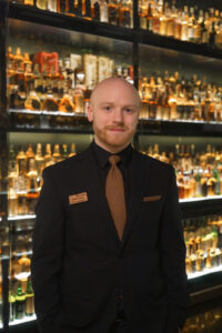 Imge of male staff member stadnign against whisky collection