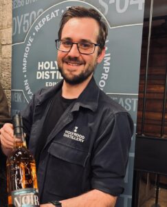 Image of male standing smiling holding up a bottle of Scotch whisky from Holyrood Distillery.