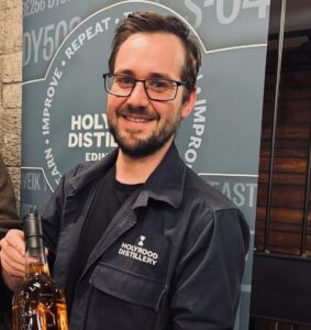 Image of male standing smiling holding up a bottle of Scotch whisky from Holyrood Distillery.