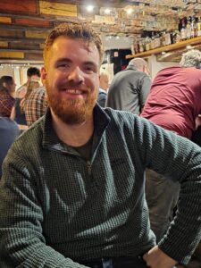Image of male sitting down in a bar and smiling to the camera.