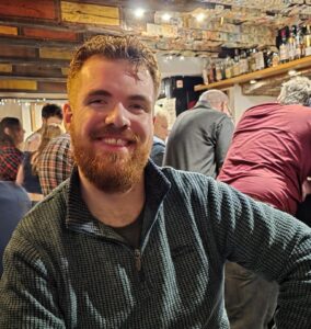 Image of male sitting down in a bar and smiling to the camera.